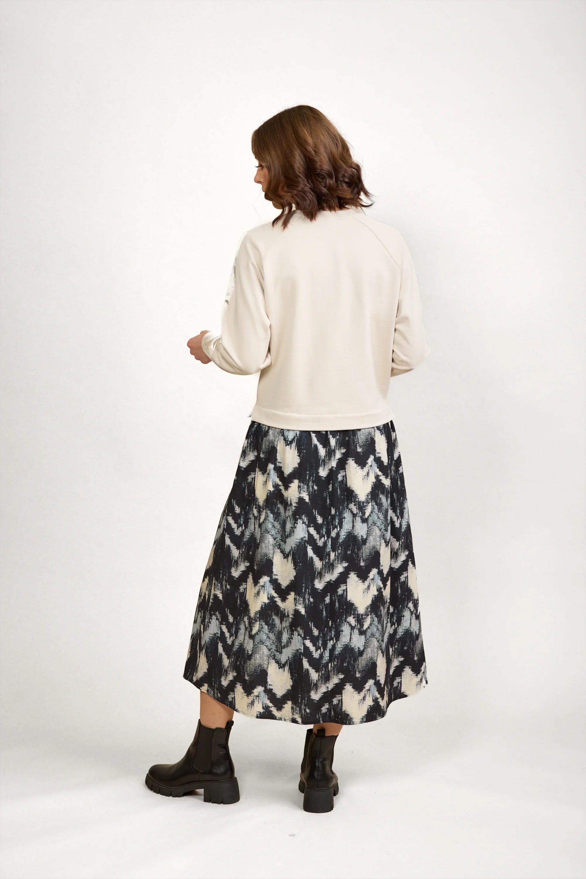 Woman in a cream sweater and abstract pattern midi skirt with black ankle boots, studio background