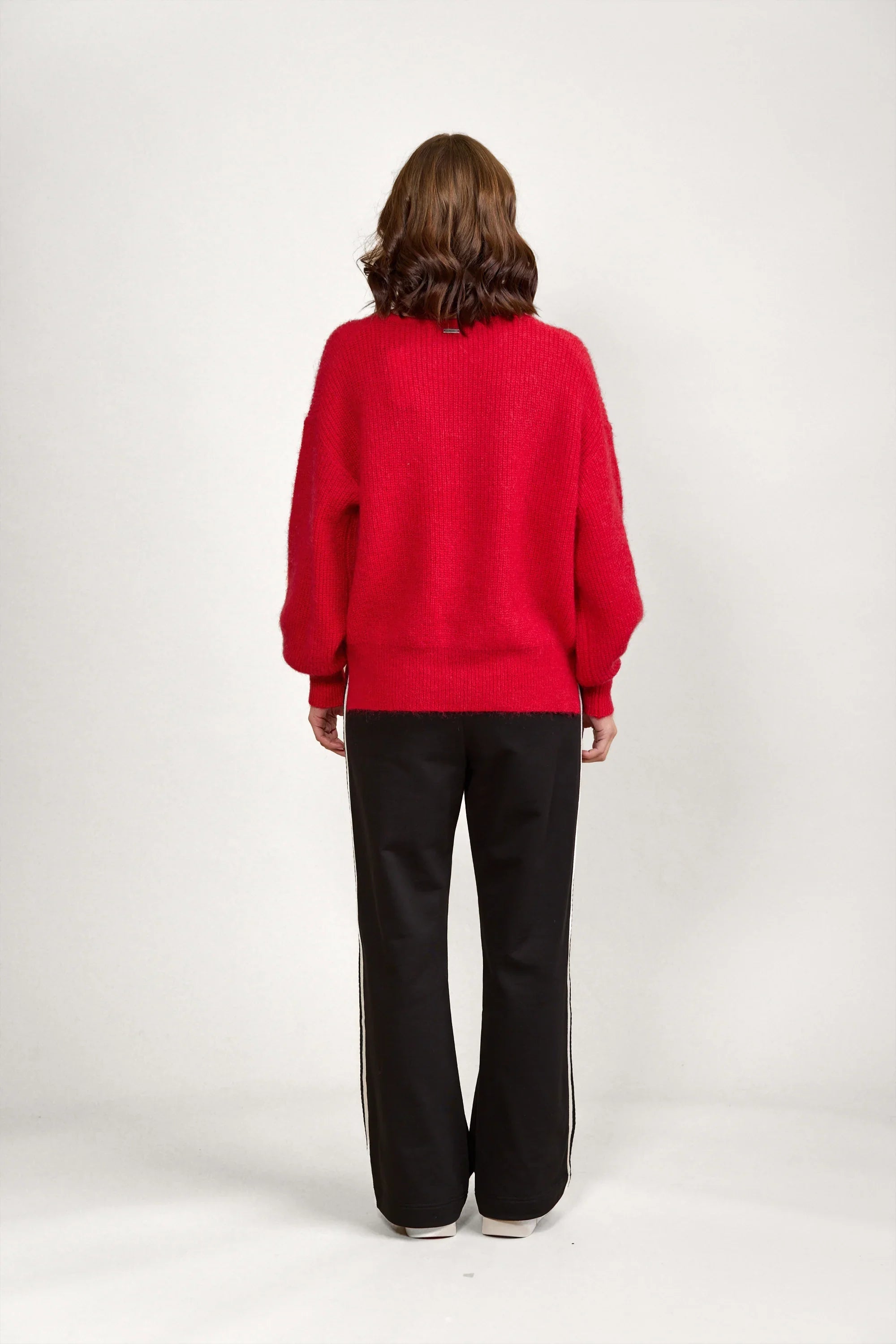 Woman wearing a red knit sweater and black pants, back view, minimalist studio setting