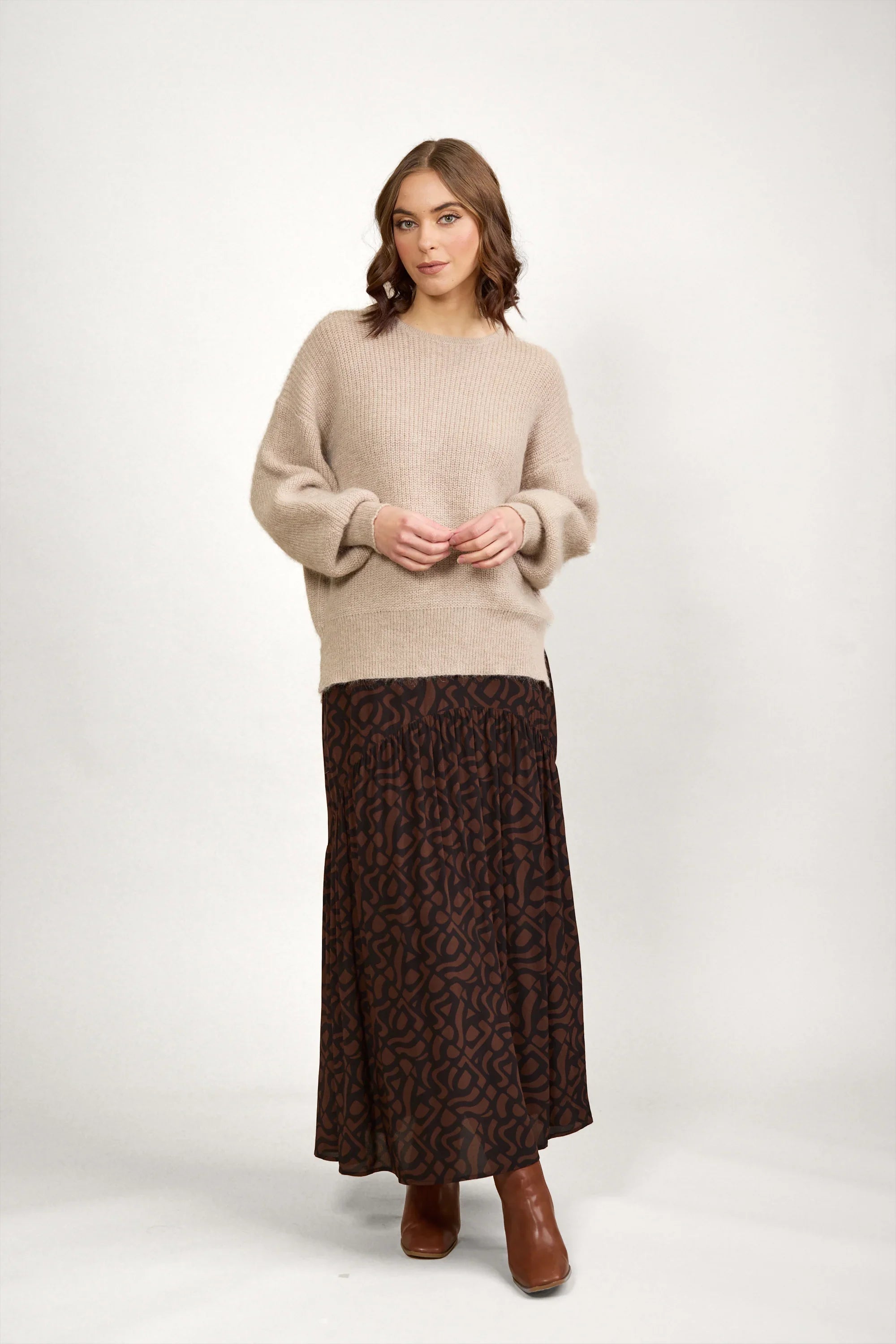 Woman wearing an oatmeal knit sweater with a patterned brown maxi skirt and brown boots