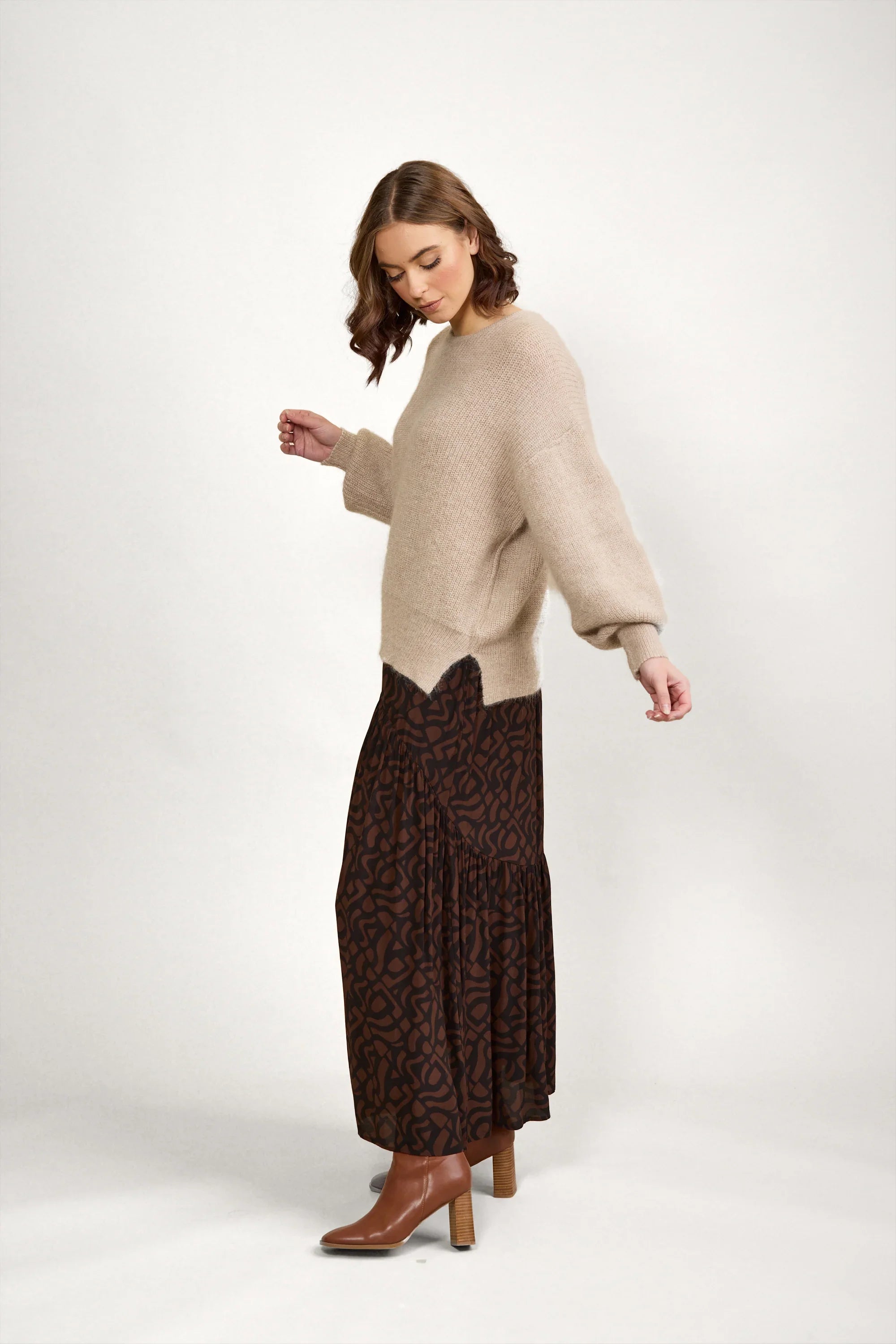 Woman in oatmeal knit sweater, brown printed maxi skirt, and tan ankle boots