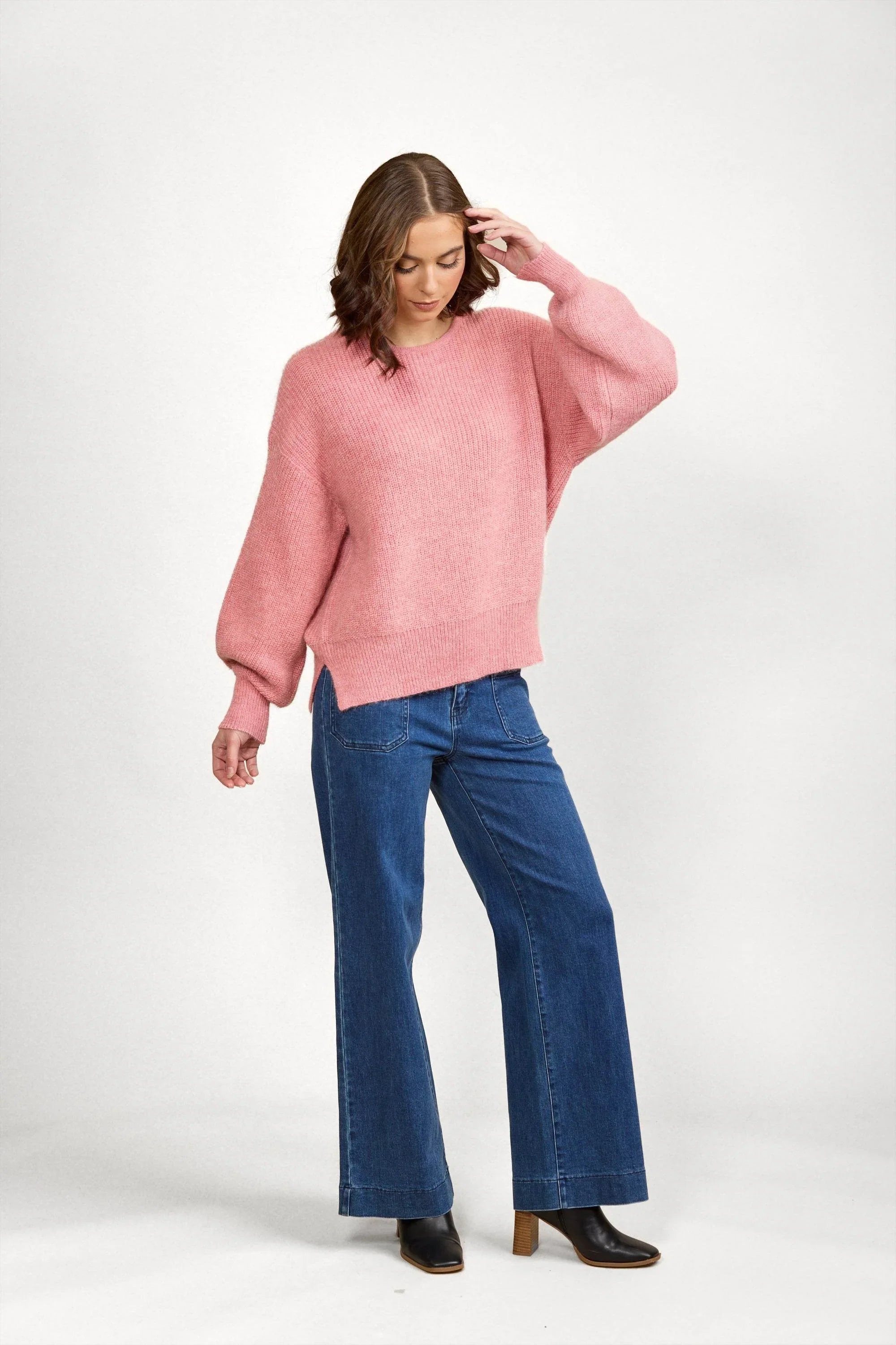 Woman wearing a loose pink knit sweater with wide-leg blue jeans and black boots