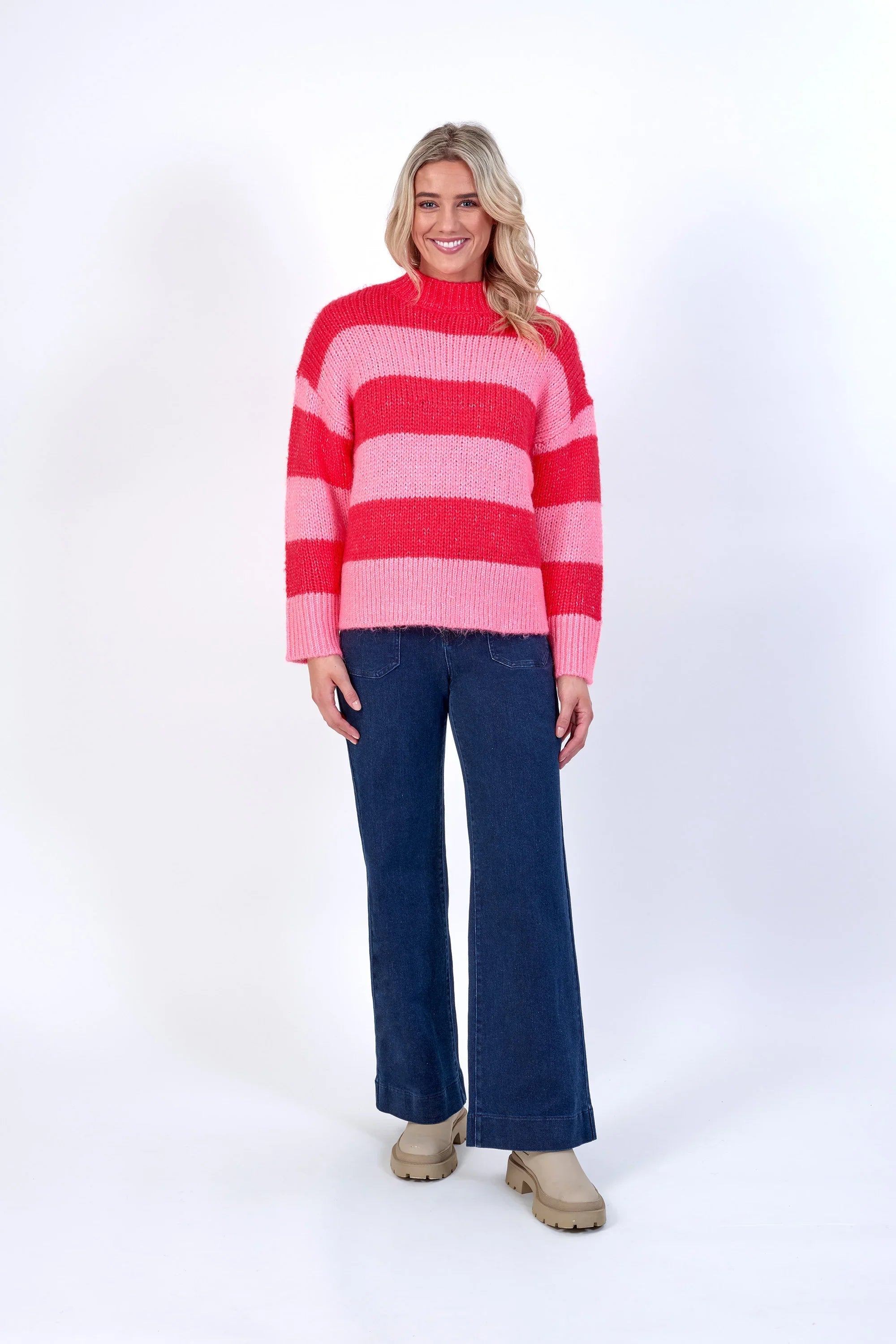 Woman wearing pink and red striped knit sweater, wide-leg jeans, and beige boots