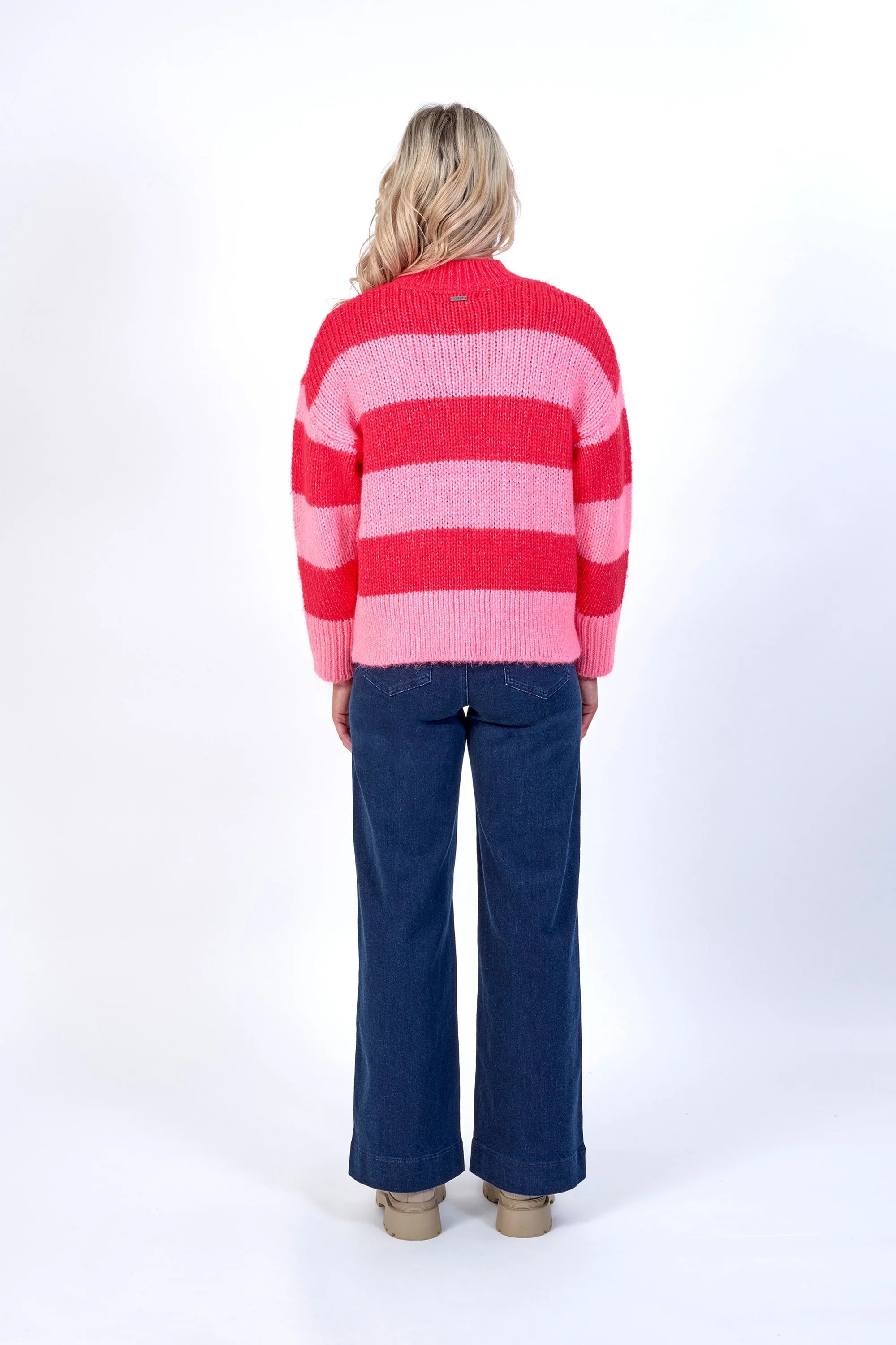 Back view of model in pink and red striped knit sweater with blue wide-leg jeans