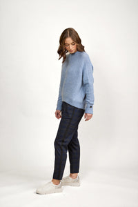 Woman wearing a sky blue knit sweater, plaid pants, and white sneakers against a plain background.