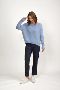 Woman wearing a sky blue knit sweater, plaid pants, and white sneakers in studio setting