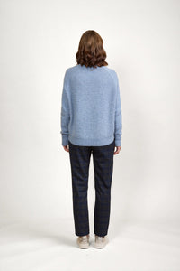 Woman wearing light blue knit sweater, checked pants, and sneakers, seen from the back