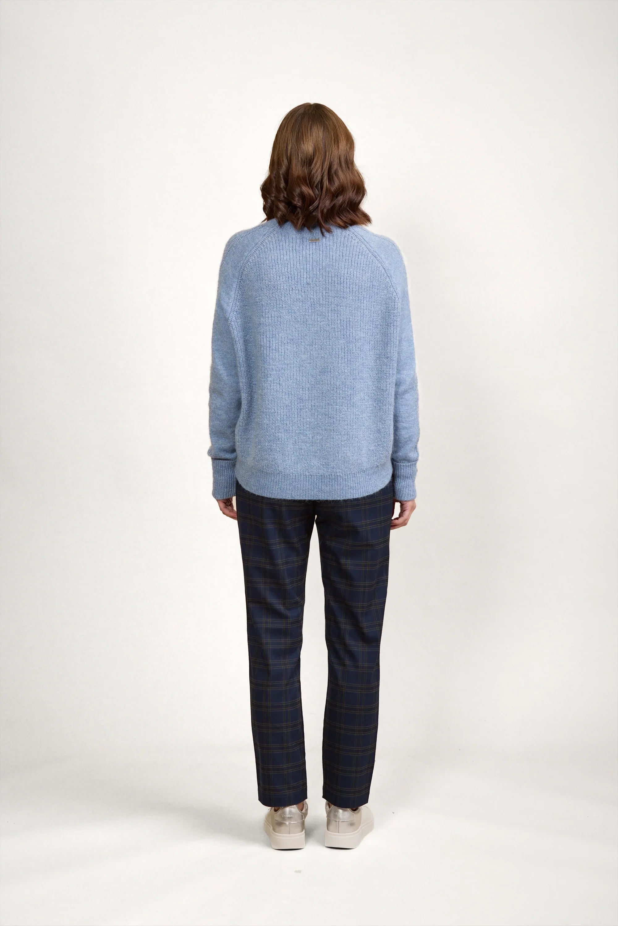 Woman wearing light blue knit sweater, checked pants, and sneakers, seen from the back
