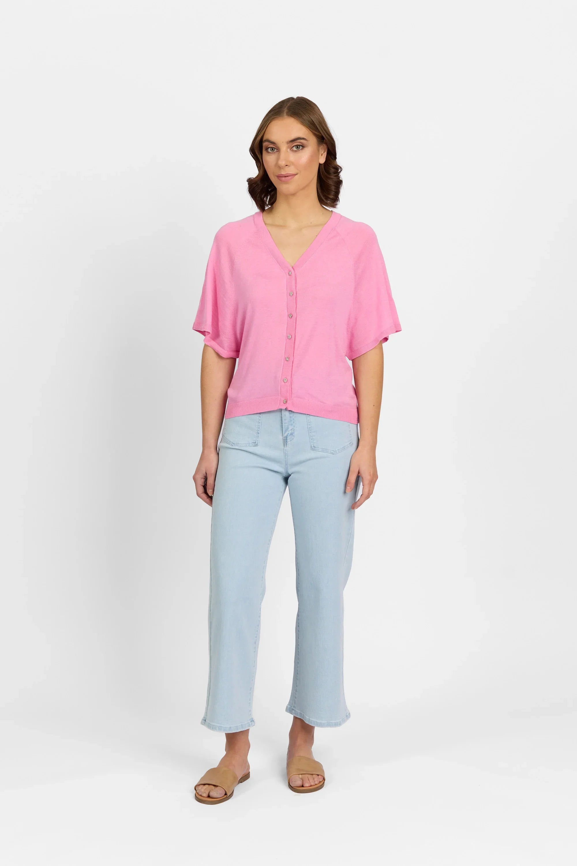 Woman wearing a pink button-up knit sweater, light wash jeans, and sandals on white background