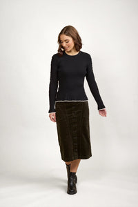 Woman wearing a black ribbed knit sweater with white trim, buttoned midi skirt, and black boots