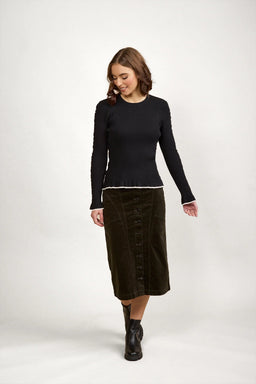 Woman wearing a black ribbed knit sweater with white trim, buttoned midi skirt, and black boots