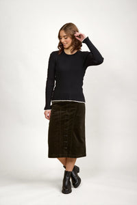 Woman wearing a black ribbed long-sleeve sweater, olive button-front midi skirt, and black boots