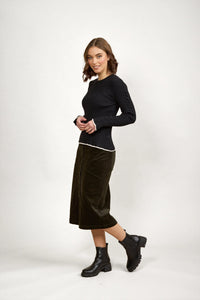 Woman wearing a fitted black knit sweater, midi skirt, and black ankle boots