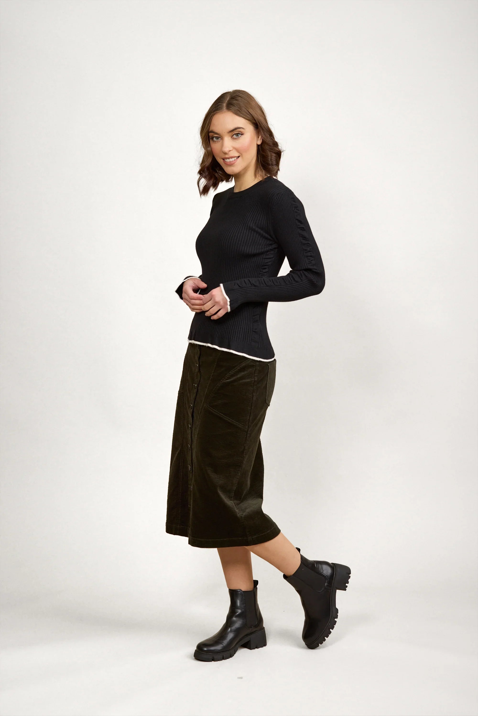 Woman wearing a fitted black knit sweater, midi skirt, and black ankle boots