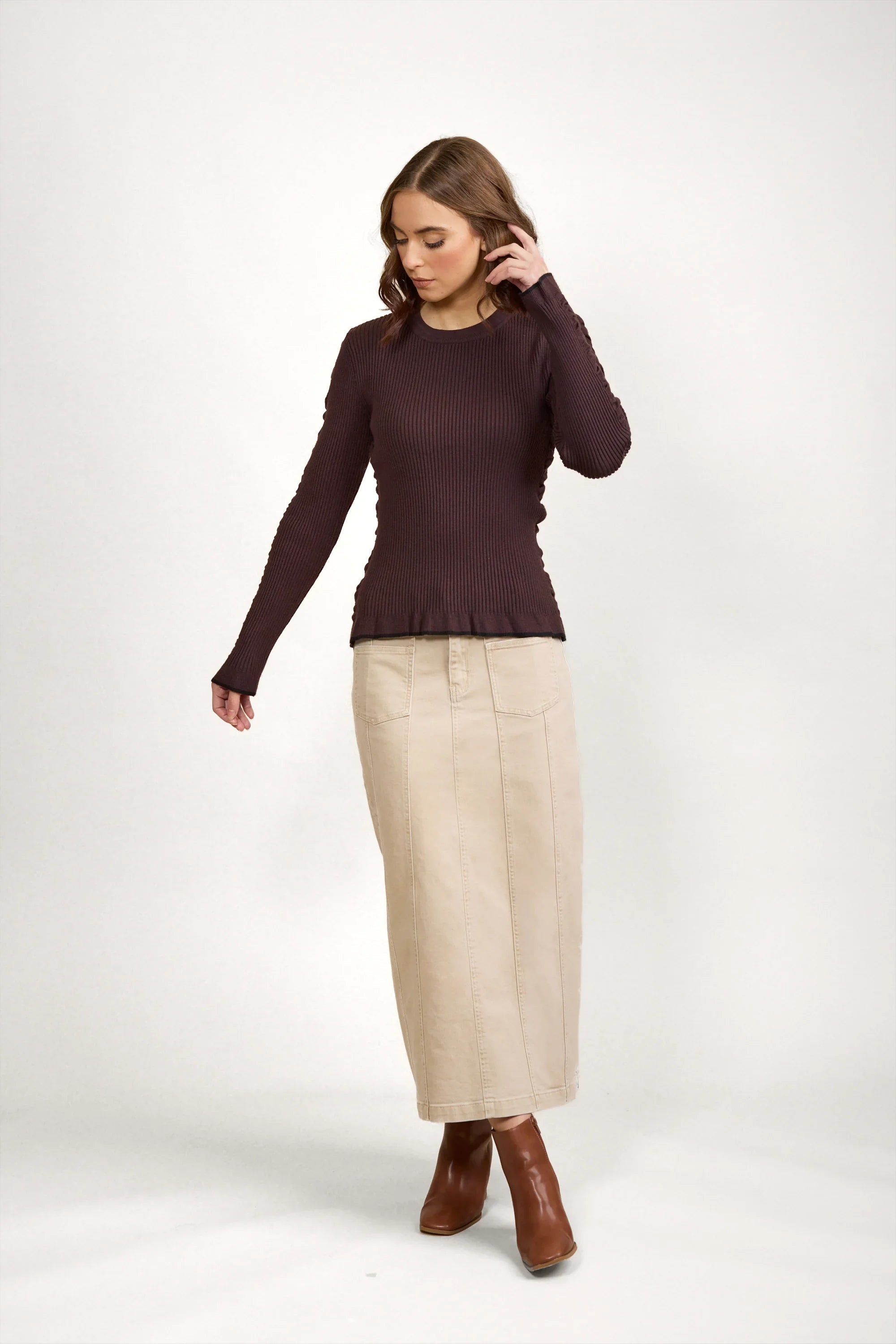 Woman wearing chocolate brown ribbed sweater with beige midi skirt and brown ankle boots