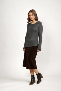 Woman wearing long sleeve grey knit sweater, brown midi skirt, and black ankle boots