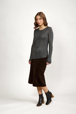 Woman wearing long sleeve grey knit sweater, brown midi skirt, and black ankle boots