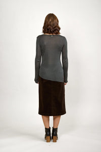 Woman in a sheer grey long sleeve sweater, brown midi skirt, and black ankle boots, back view