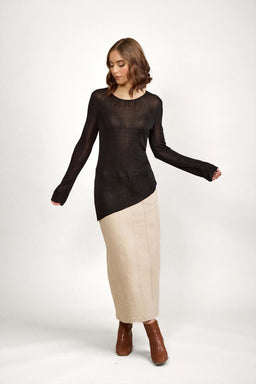 Woman wearing black sheer knit sweater, beige maxi skirt, and brown ankle boots