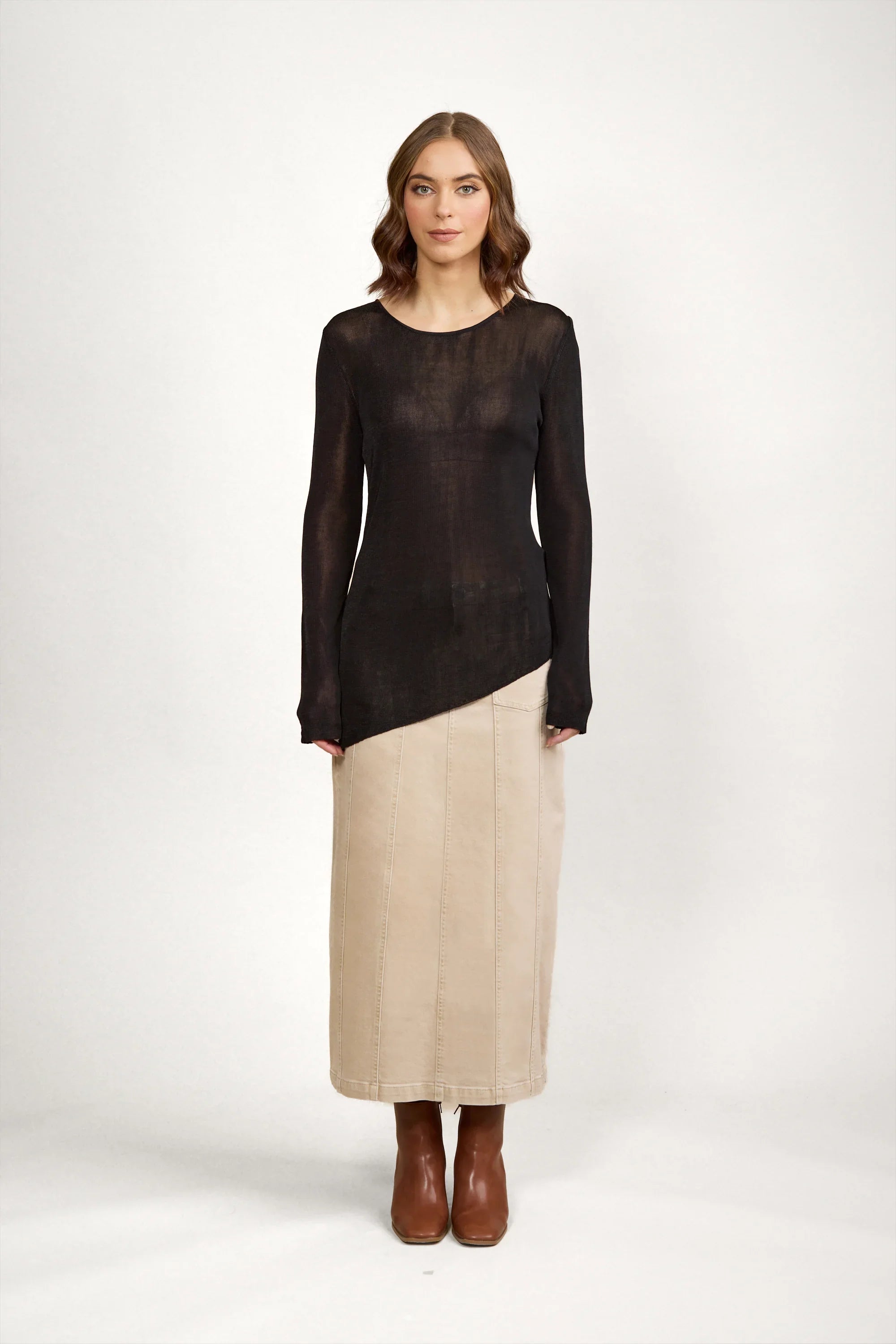 Woman wearing black sheer long sleeve sweater with beige midi skirt and brown boots