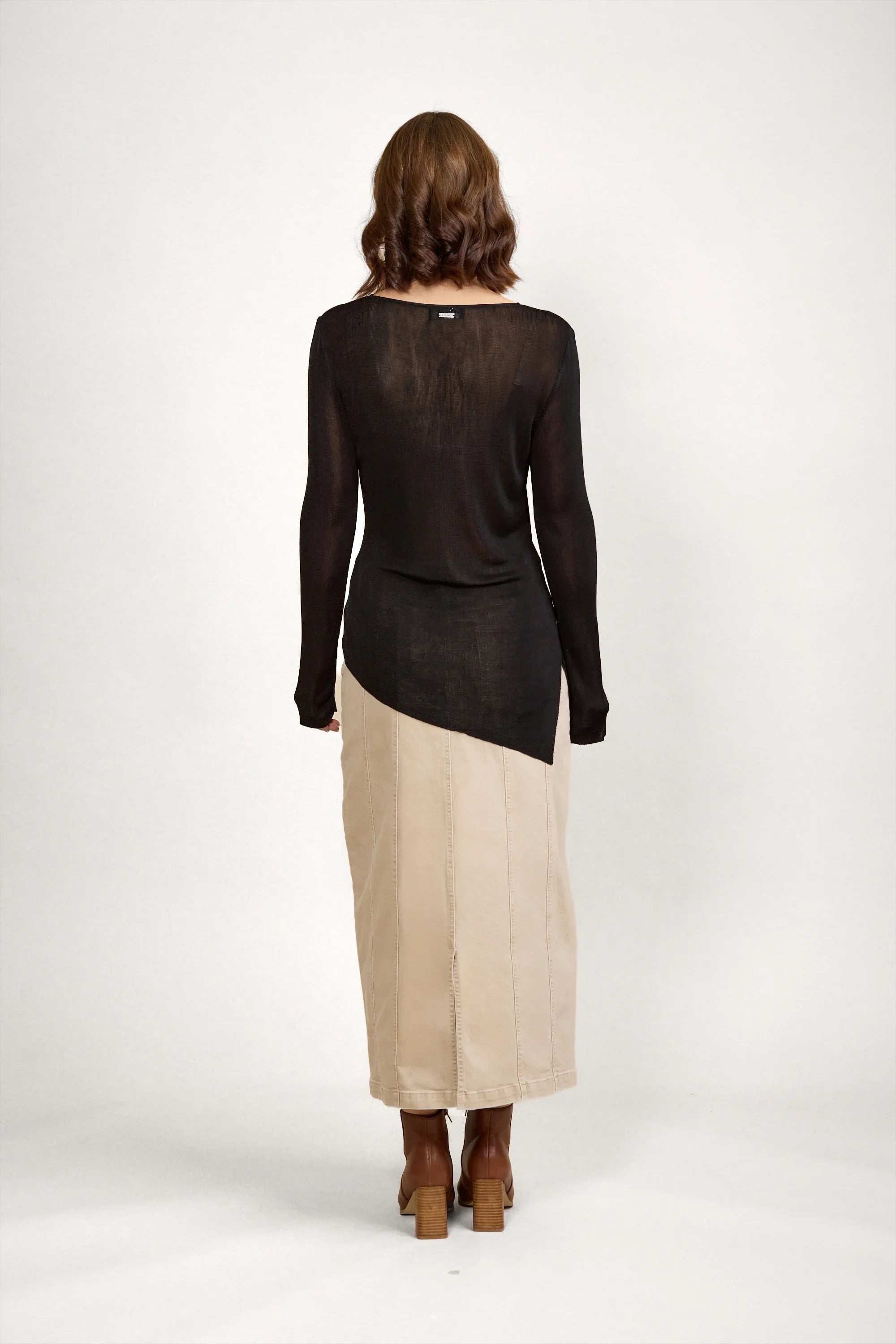 Woman wearing black long sleeve sweater and beige maxi skirt, back view, neutral background
