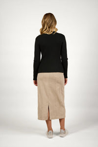 Woman modeling a black ribbed sweater and beige midi skirt, back view, neutral background
