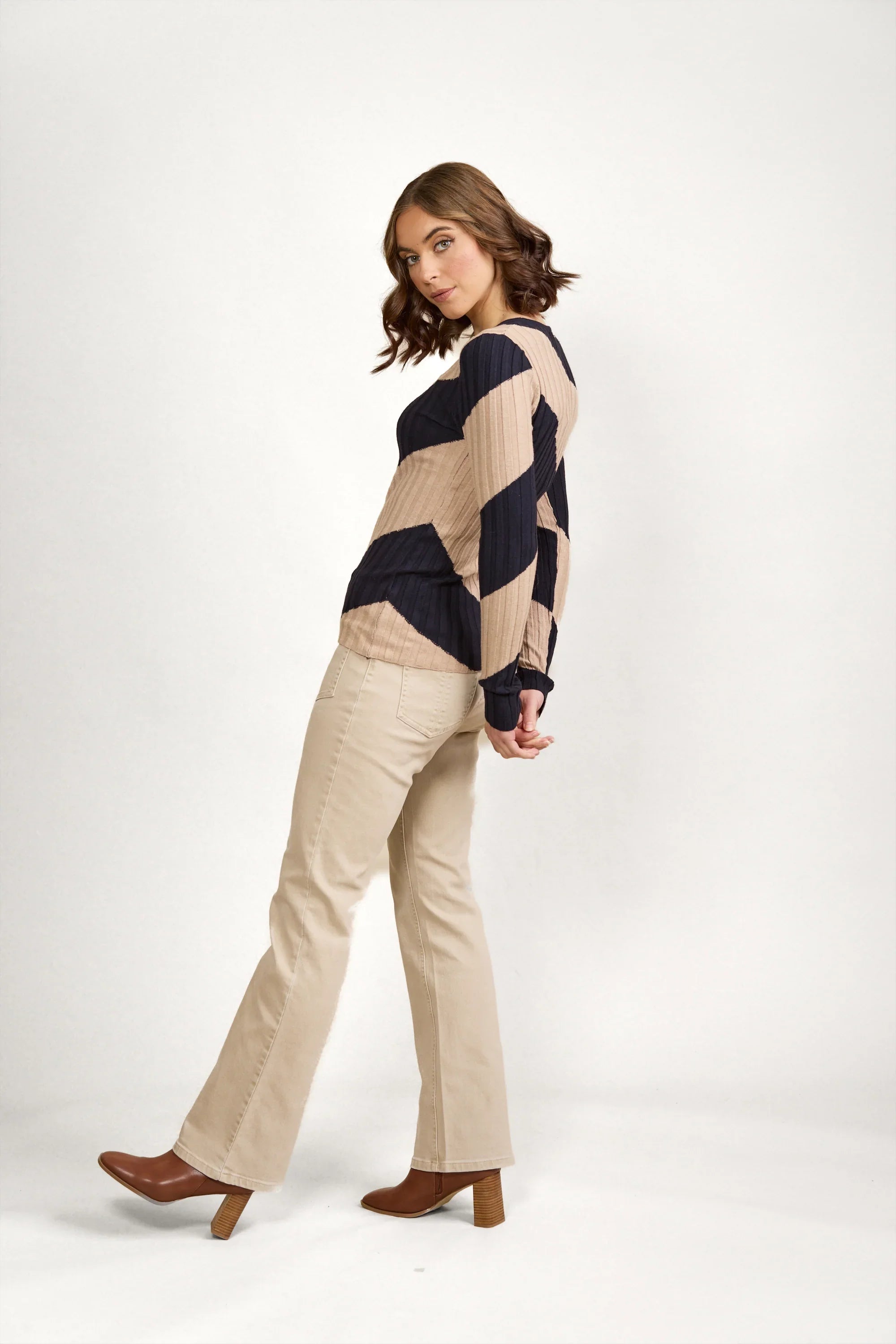 Woman wearing a navy and beige geometric knit sweater with beige pants and brown boots