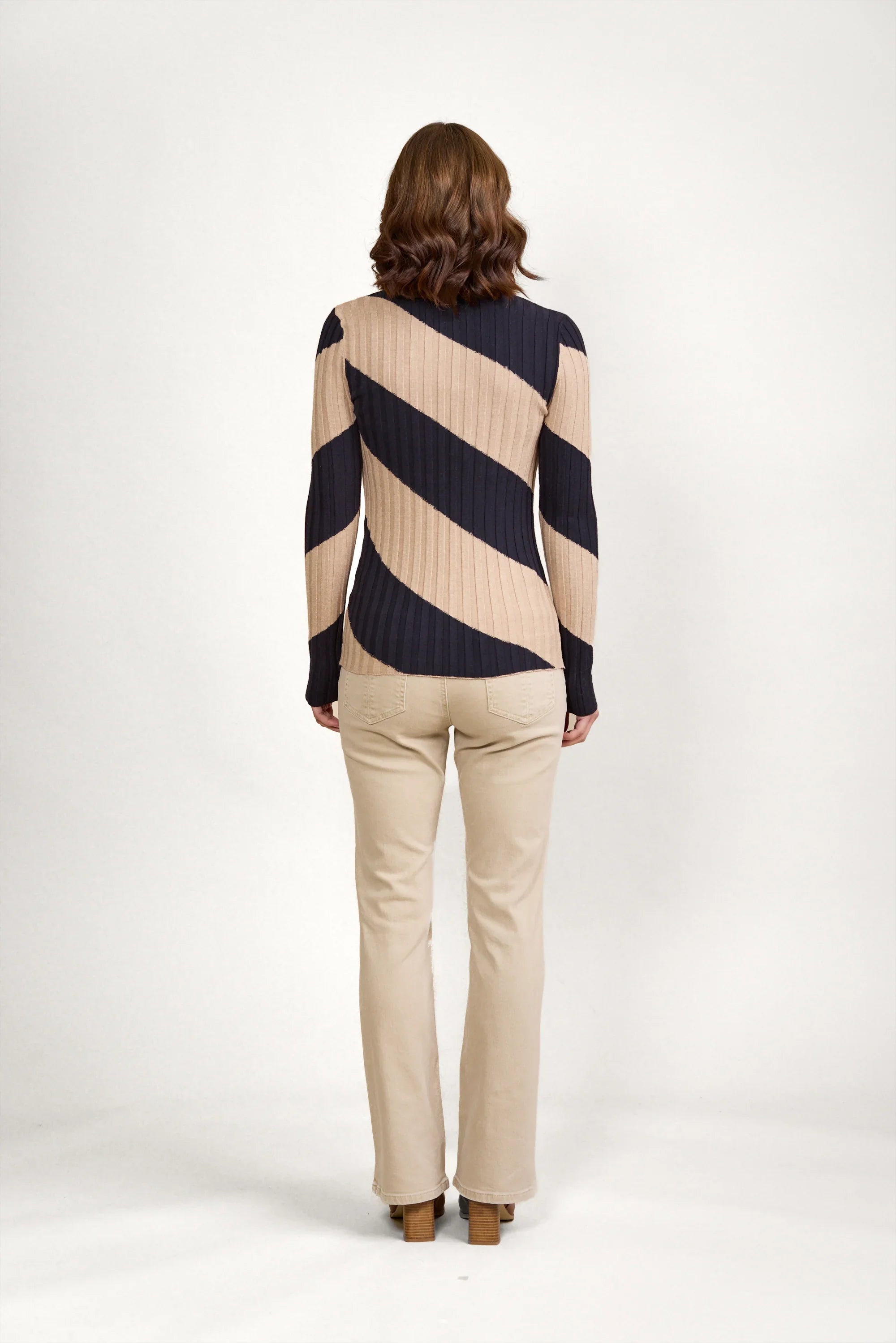 Woman in ribbed knit sweater with navy and beige diagonal stripes, beige pants, studio background