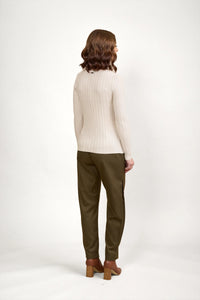 Woman wearing an oatmeal ribbed sweater and olive pants, back view, studio setting