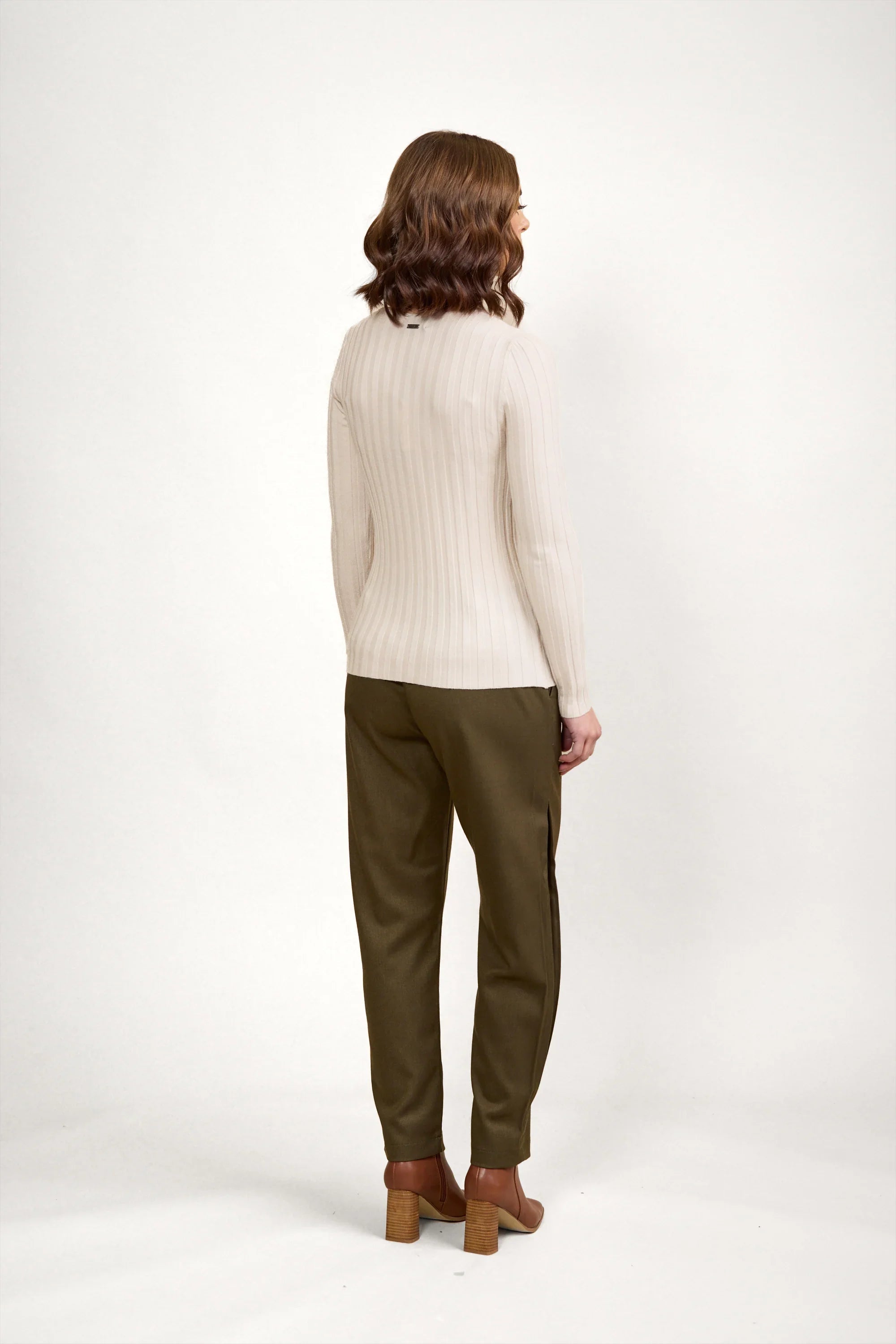 Woman wearing an oatmeal ribbed sweater and olive pants, back view, studio setting