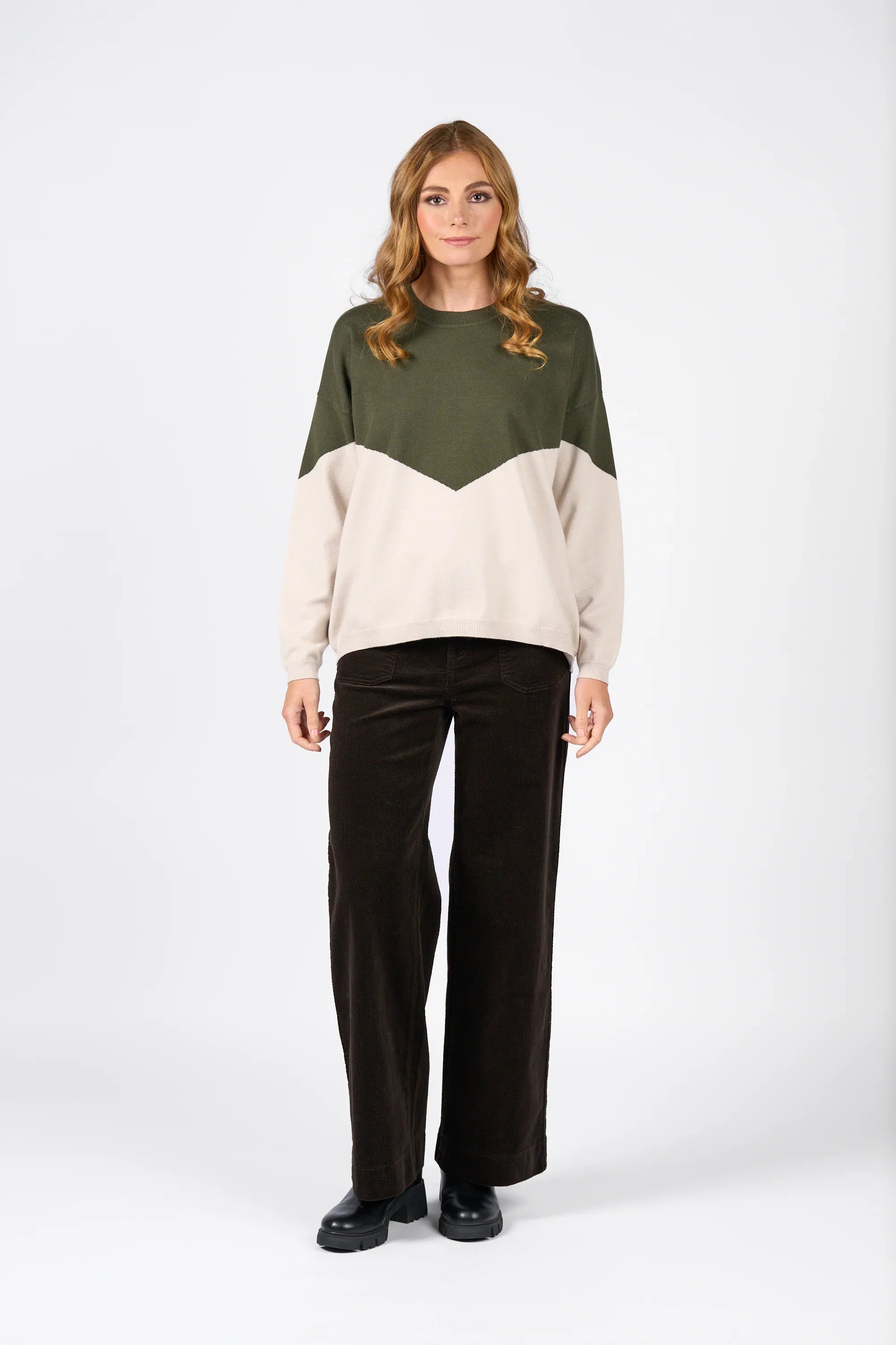 Woman in an olive green and oatmeal color block knit sweater with brown wide-leg pants