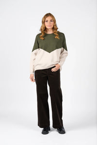 Woman wearing a hunter green and oatmeal colorblock knit sweater with wide-leg dark trousers