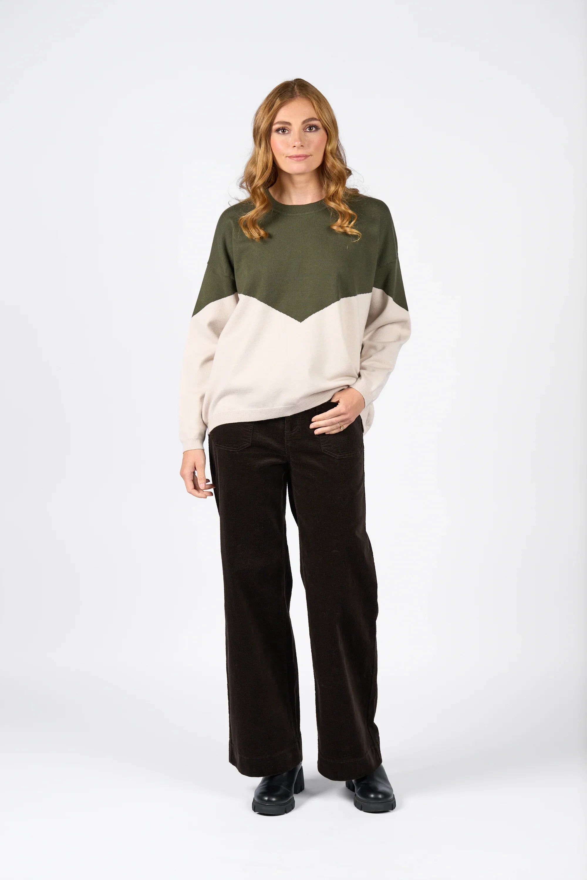 Woman wearing a hunter green and oatmeal colorblock knit sweater with wide-leg dark trousers