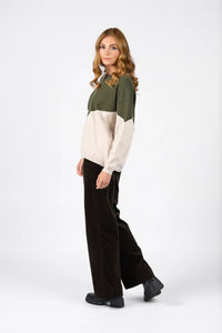 Woman wearing colorblock hunter green and oatmeal sweater with wide leg dark pants