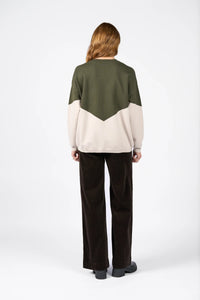 Back view of a woman wearing a green and oatmeal colorblock knit sweater and dark pants