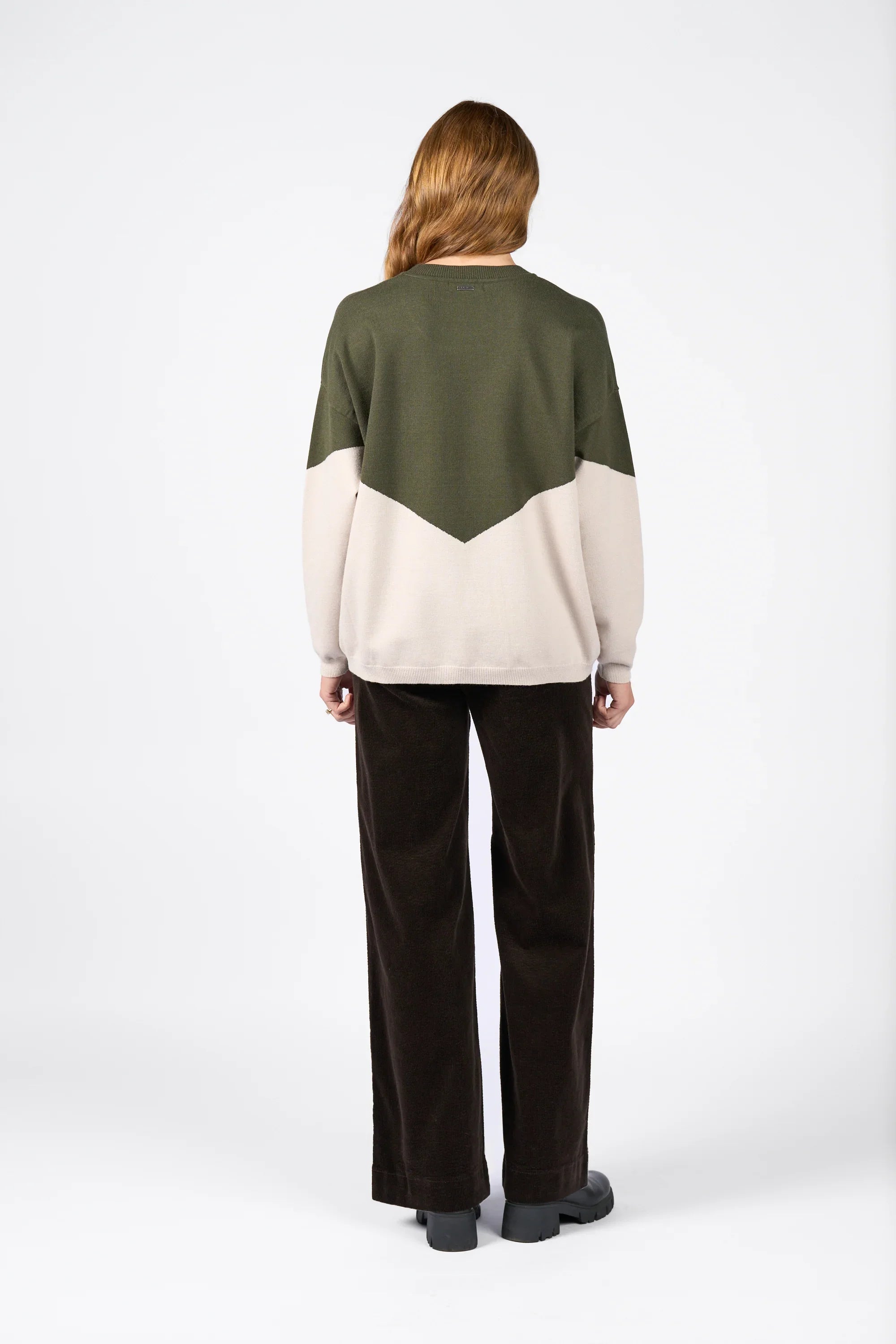 Back view of a woman wearing a green and oatmeal colorblock knit sweater and dark pants