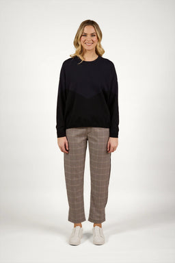 Woman wearing a black knit sweater with checkered pants and white sneakers standing against a plain background.