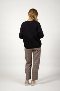 Woman in black knit sweater and checked pants, back view, studio background