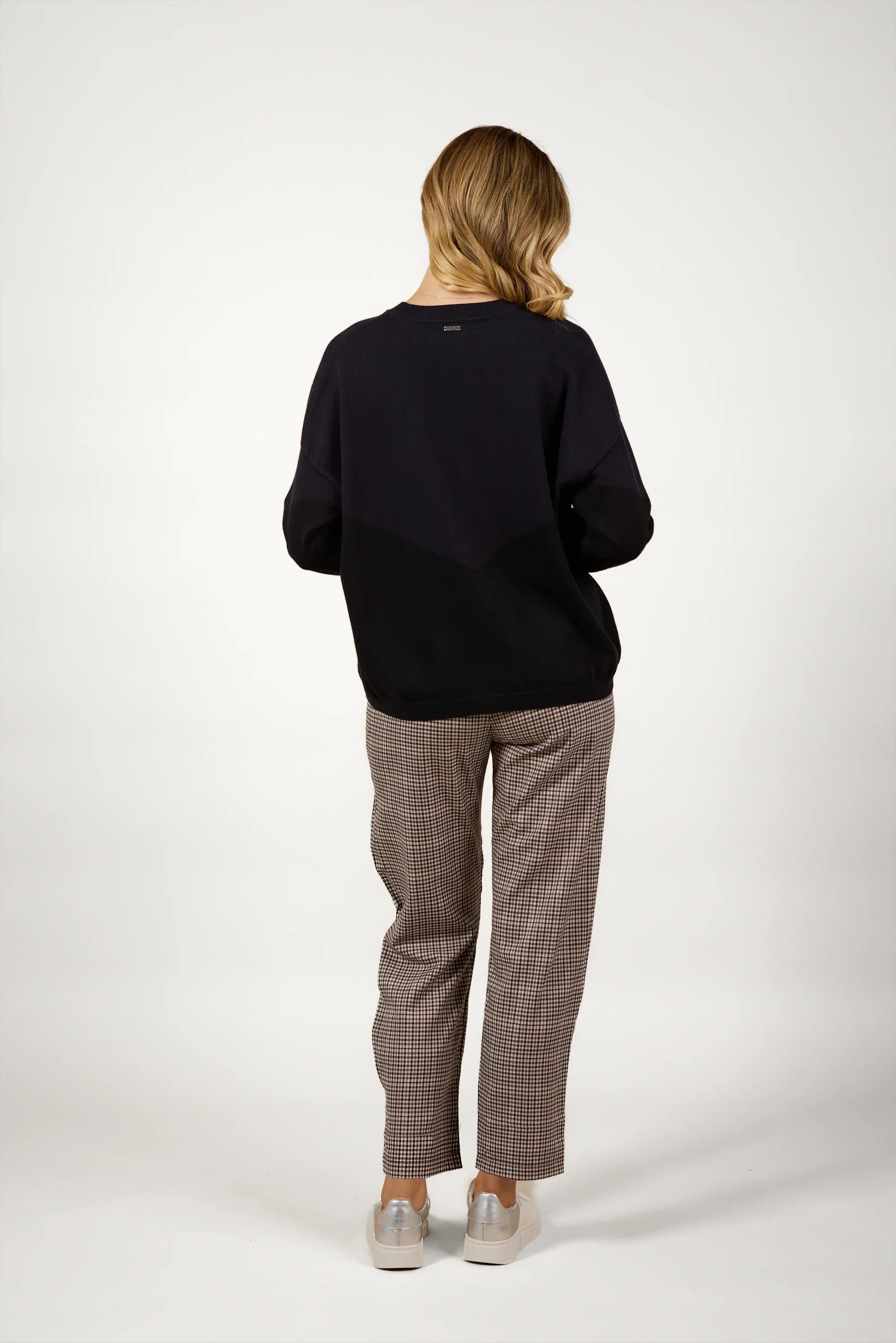 Woman in black knit sweater and checked pants, back view, studio background