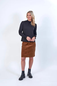Woman wearing a black long sleeve blouse, brown corduroy skirt, and black ankle boots