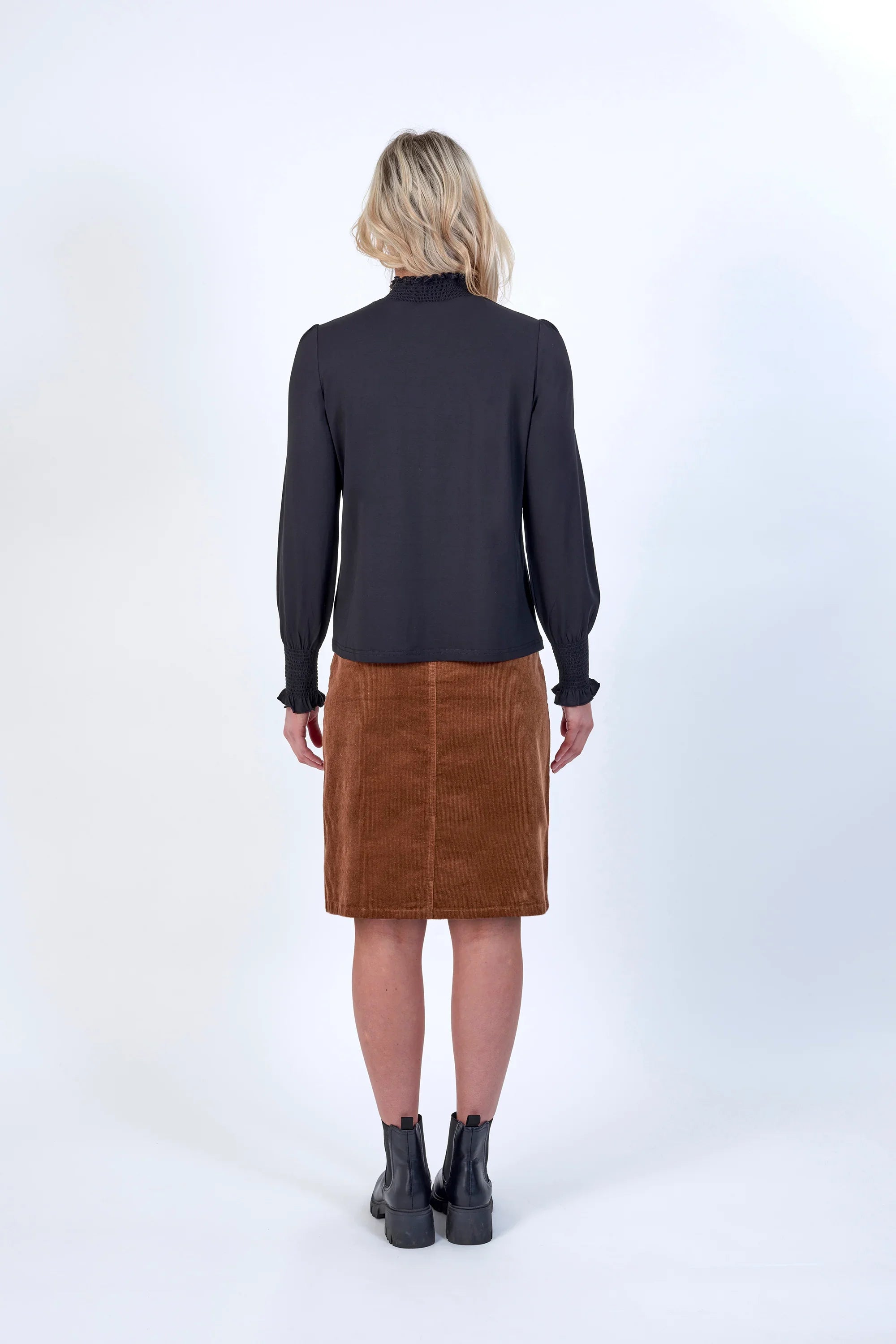 Woman in black long sleeve blouse and brown knee-length skirt, back view