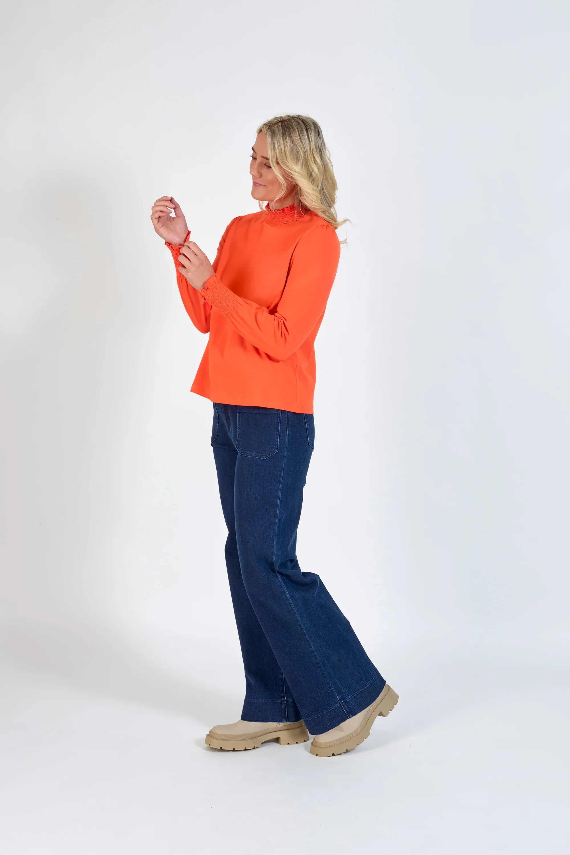 Woman wearing an orange long sleeve top with shirred cuffs and dark blue wide-leg jeans