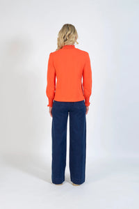 Woman in bright orange long sleeve top with smocked cuffs and dark blue wide-leg jeans, back view
