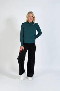Woman wearing a dark green long sleeve blouse, black wide-leg pants, and white sneakers
