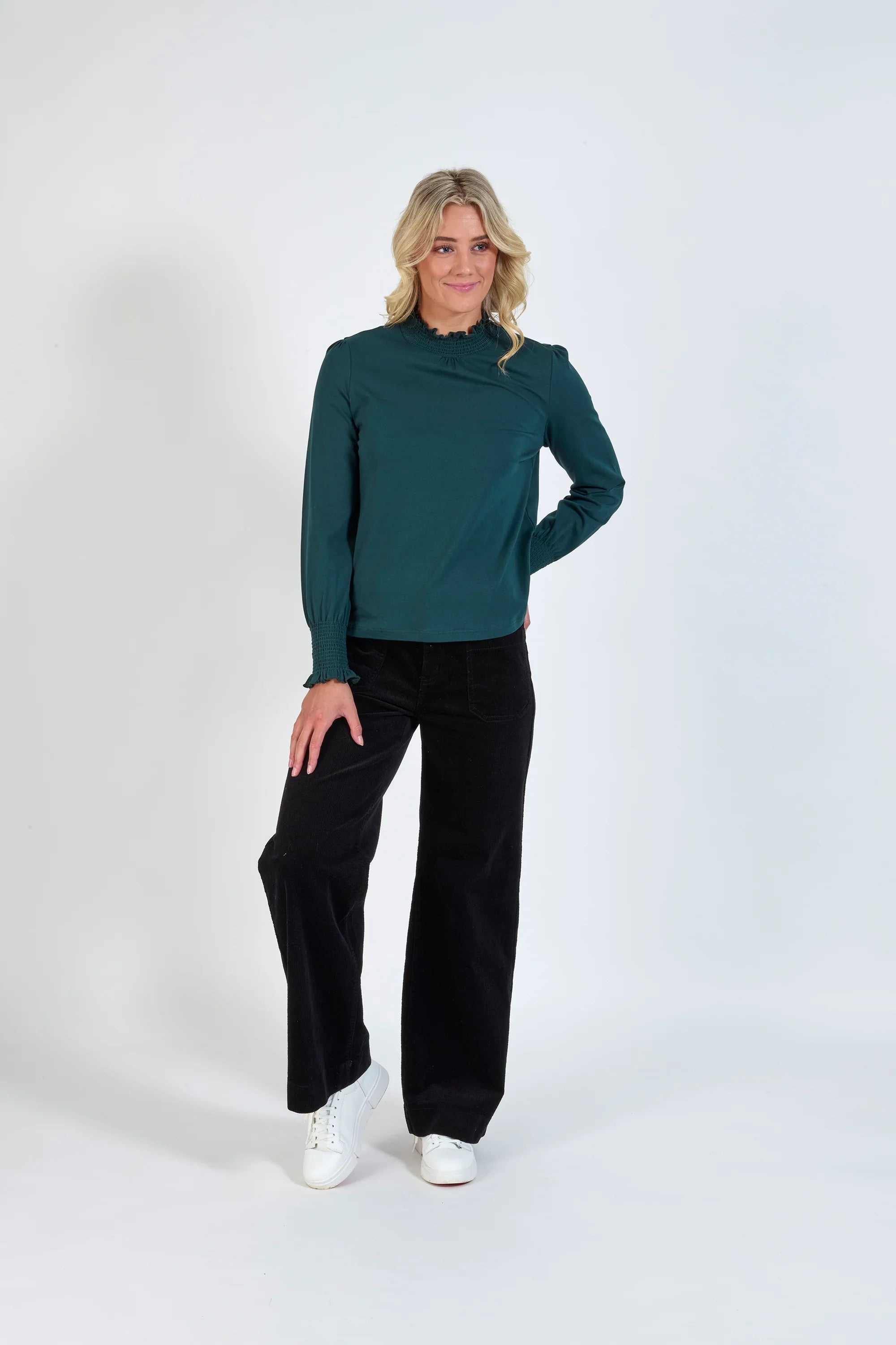 Woman wearing a dark green long sleeve blouse, black wide-leg pants, and white sneakers
