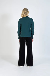 Back view of a woman wearing a long sleeve dark green top and black wide-leg pants