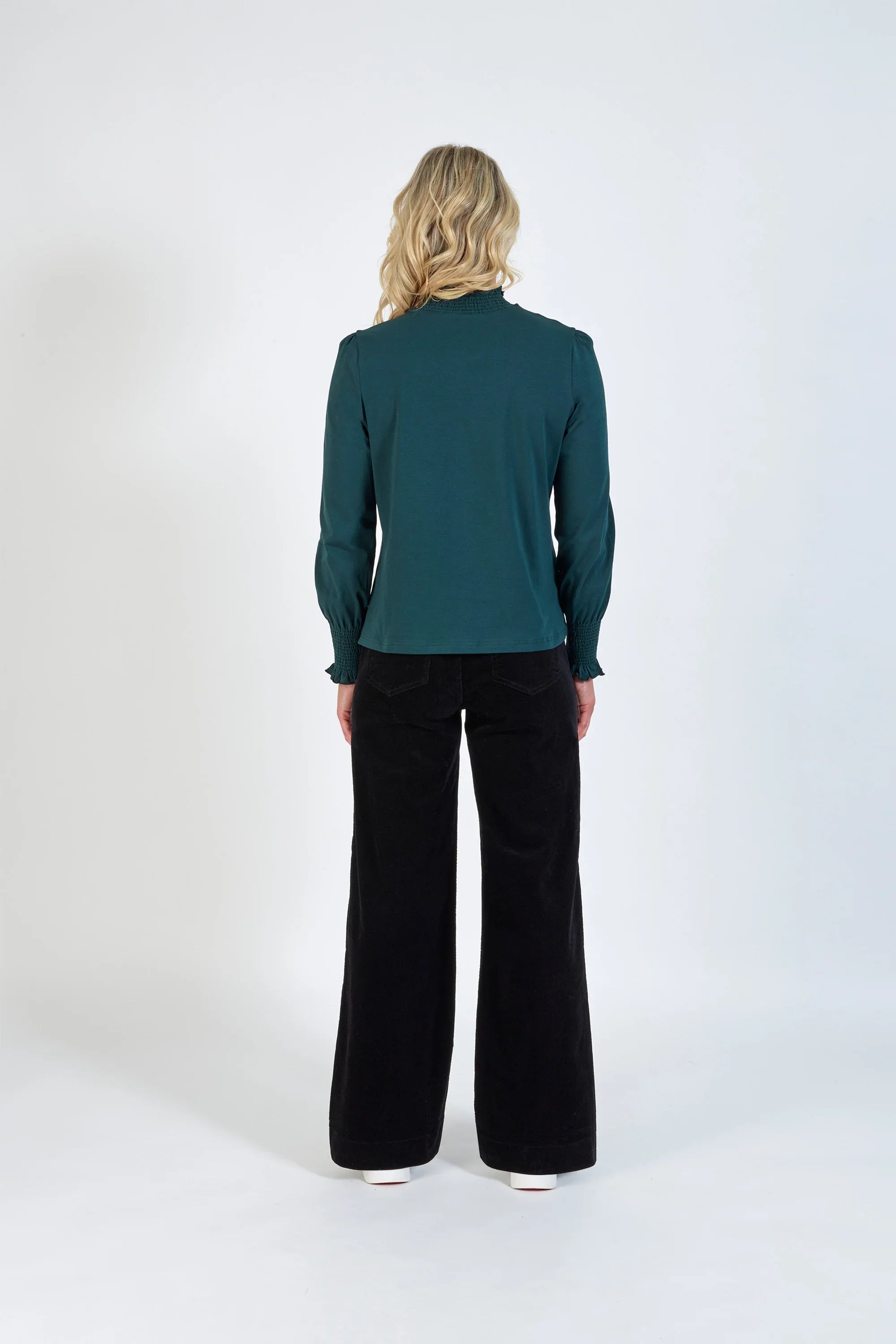 Back view of a woman wearing a long sleeve dark green top and black wide-leg pants
