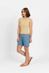 Woman wearing a colorful striped tank top, denim shorts, and orange sandals against white background