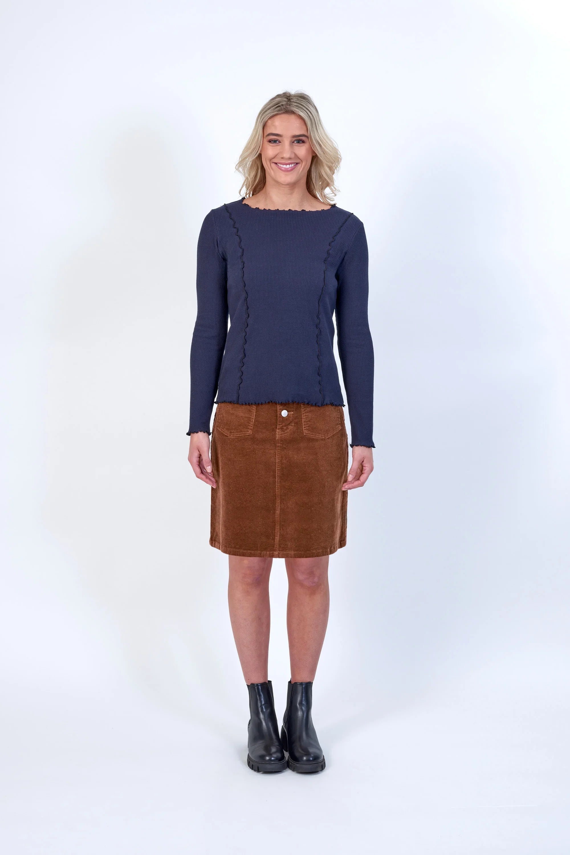 Woman wearing navy long sleeve top with textured seams, brown corduroy skirt, black boots
