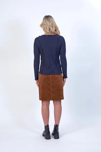 Woman wearing navy long sleeve top with wavy seams, brown corduroy skirt, black boots