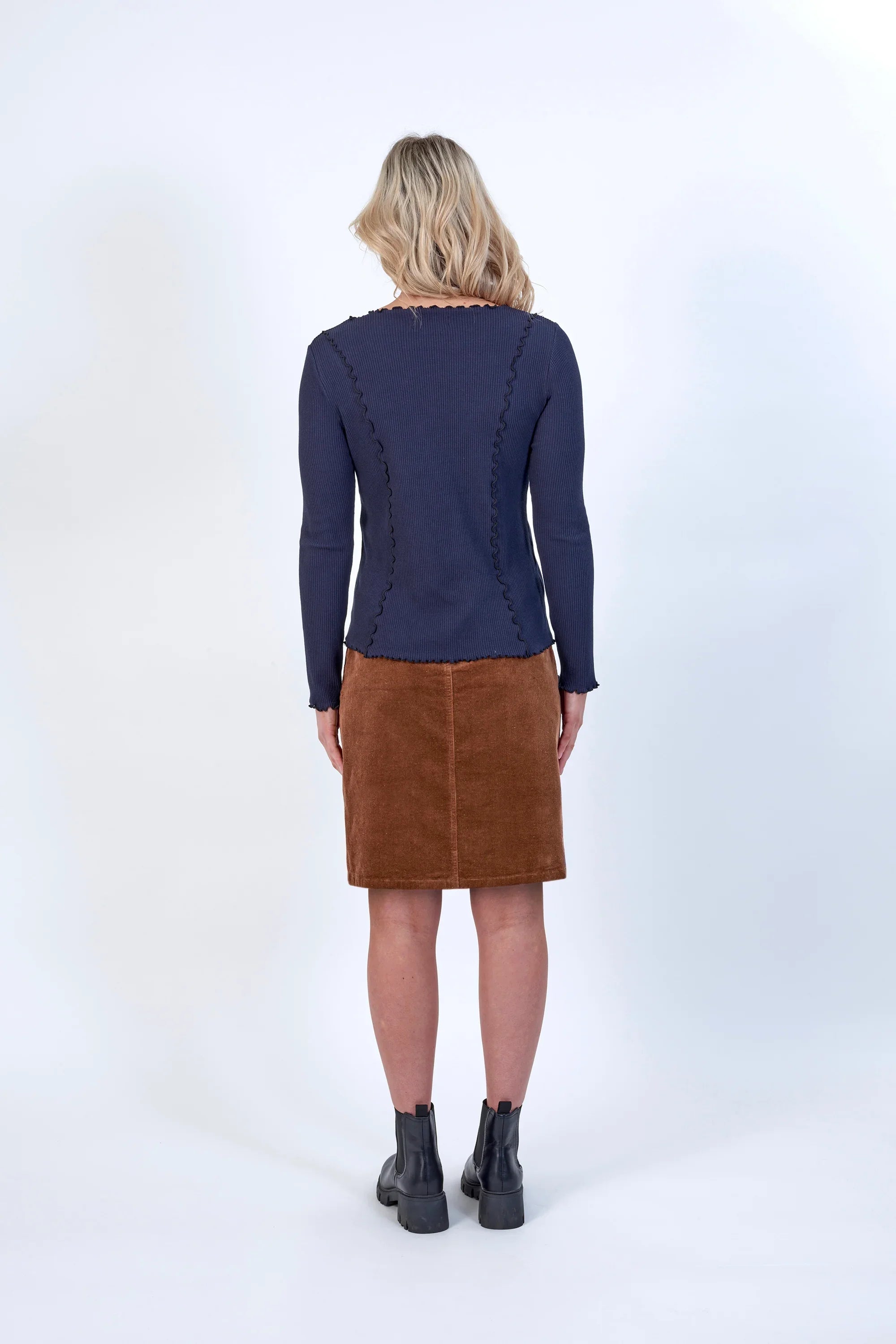 Woman wearing navy long sleeve top with wavy seams, brown corduroy skirt, black boots